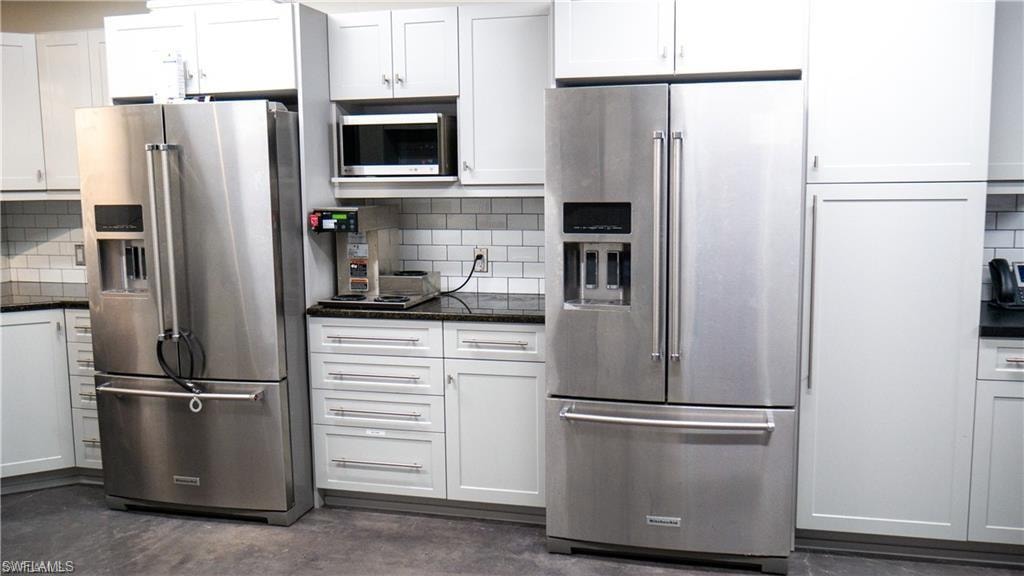 Kitchen featuring dark stone countertops, concrete floors, white cabinets, appliances with stainless steel finishes, and tasteful backsplash