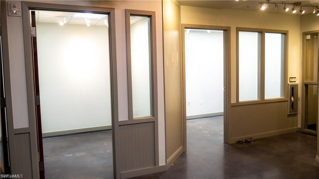 Corridor with track lighting, finished concrete flooring, and baseboards