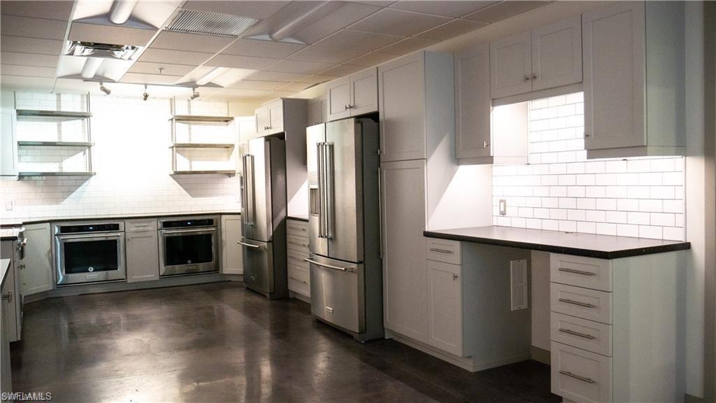 Kitchen with open shelves, backsplash, dark countertops, and appliances with stainless steel finishes