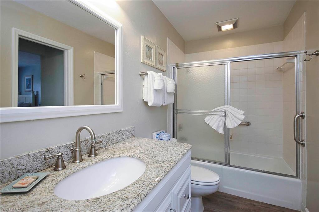 Full bath with bath / shower combo with glass door, wood finished floors, vanity, and toilet