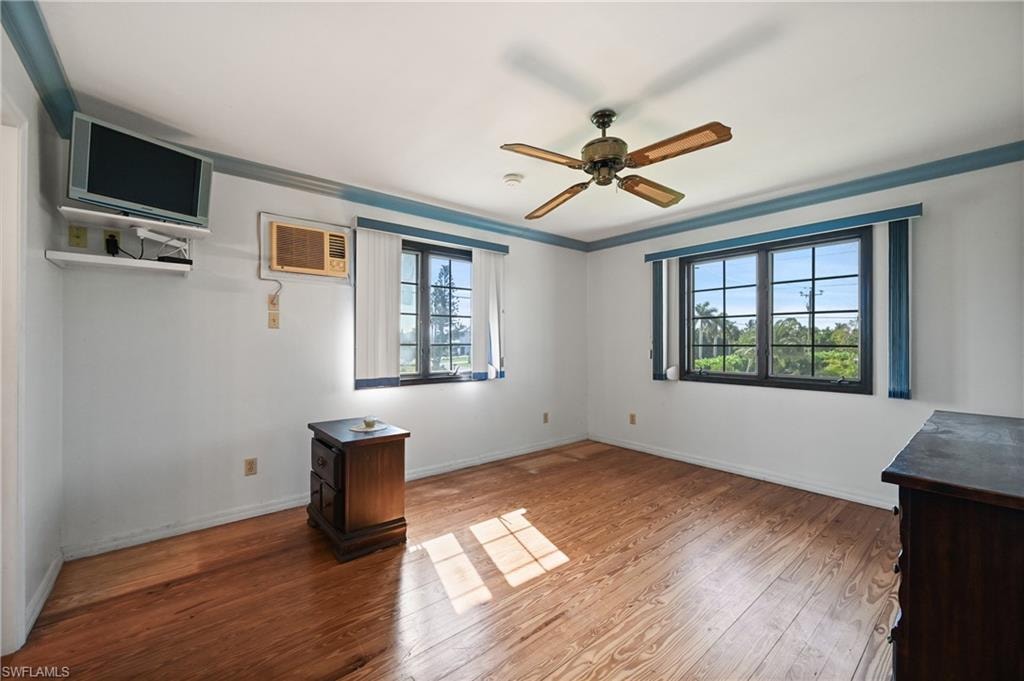 Unfurnished room featuring wood finished floors, ceiling fan, ornamental molding, and a wall unit AC