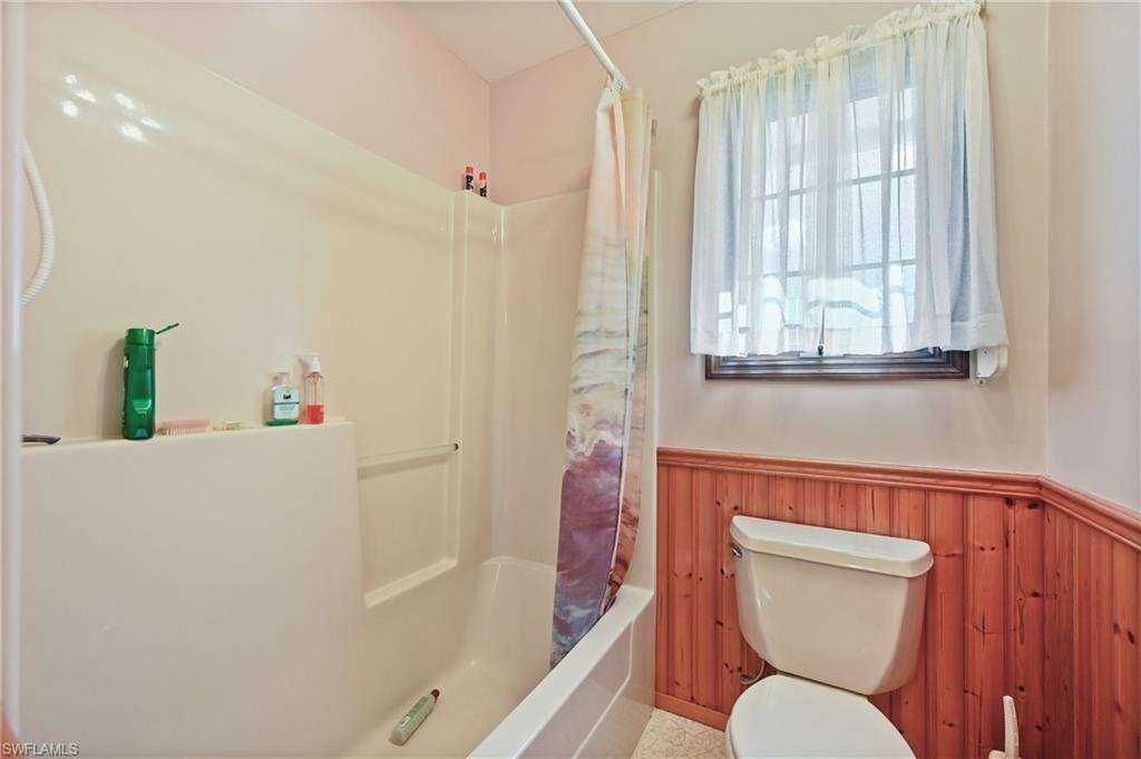 Bathroom featuring wainscoting, shower / bath combo with shower curtain, and wood walls
