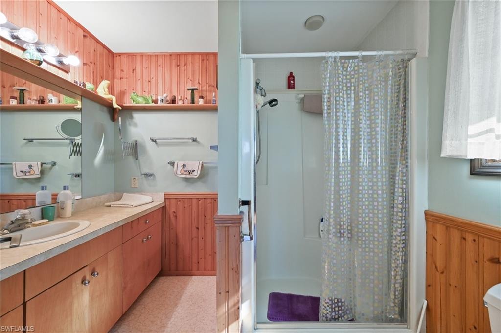 Bathroom featuring wooden walls, a wainscoted wall, a shower stall, and vanity
