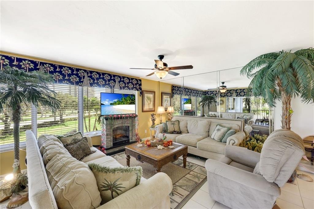 Living area featuring light tile patterned floors, a fireplace with raised hearth, and ceiling fan