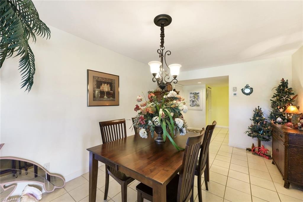 Dining space with light tile patterned floors, baseboards, and a notable chandelier