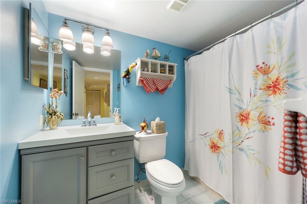 Bathroom featuring vanity, a shower with curtain, visible vents, tile patterned floors, and toilet