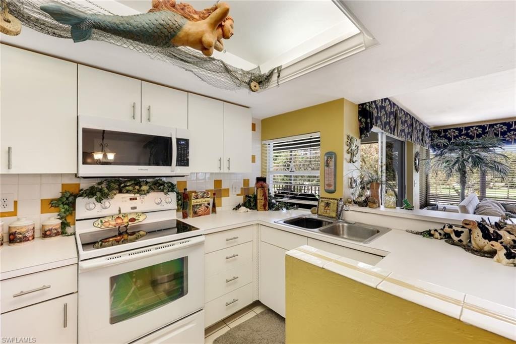 Kitchen featuring a sink, backsplash, white appliances, white cabinets, and light countertops