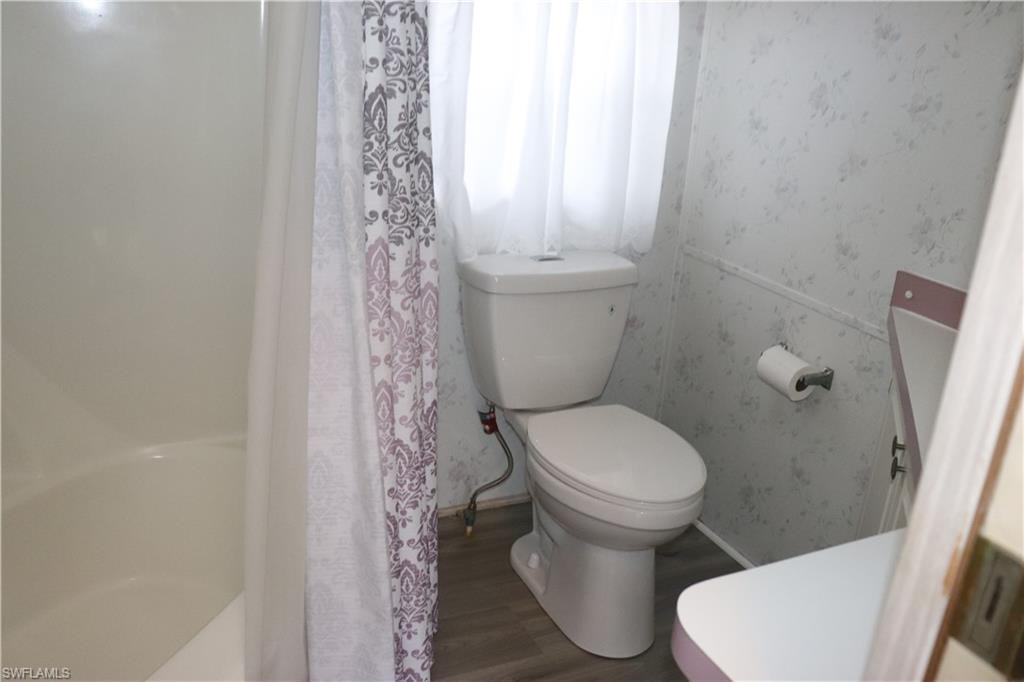 Full bath featuring a shower with curtain, wallpapered walls, toilet, and wood finished floors
