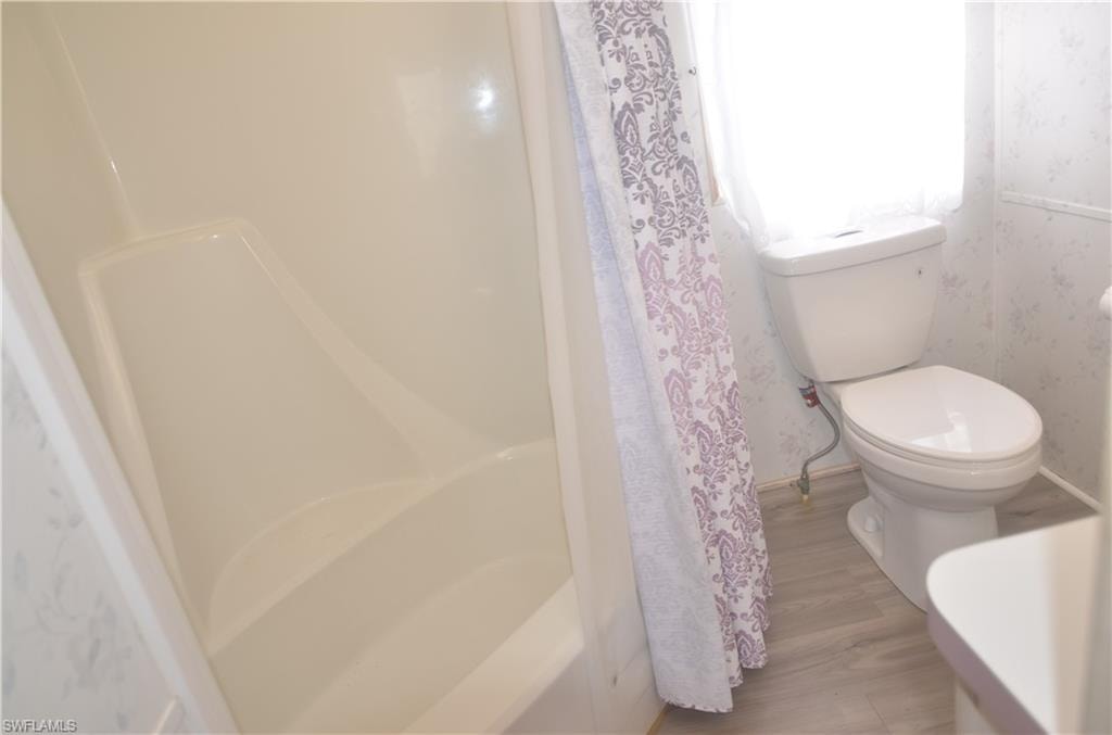 Bathroom featuring toilet, wallpapered walls, and wood finished floors