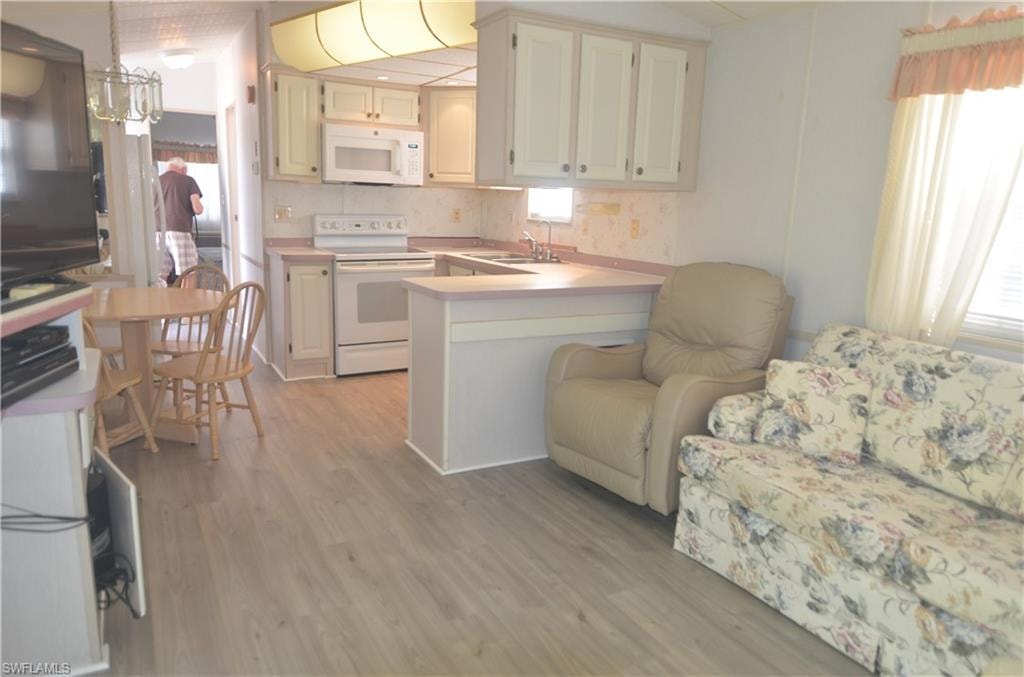 Kitchen with light countertops, light wood-type flooring, white appliances, backsplash, and a peninsula