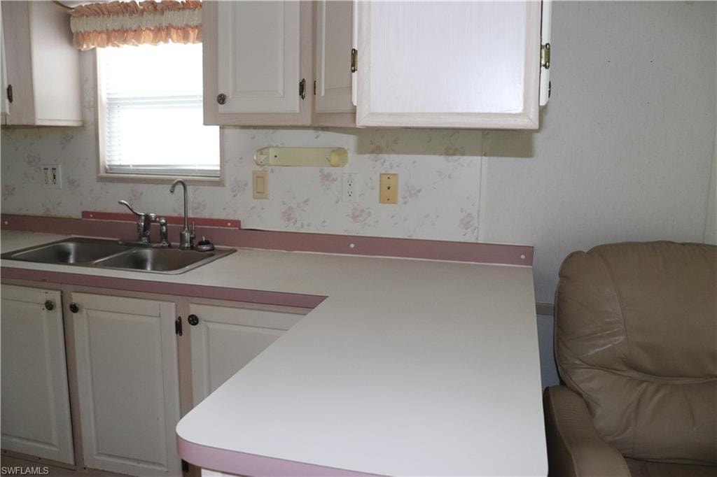 Kitchen featuring wallpapered walls, light countertops, a sink, and white cabinets