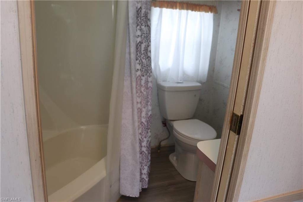 Full bath featuring a bathing tub, toilet, wood finished floors, vanity, and curtained shower