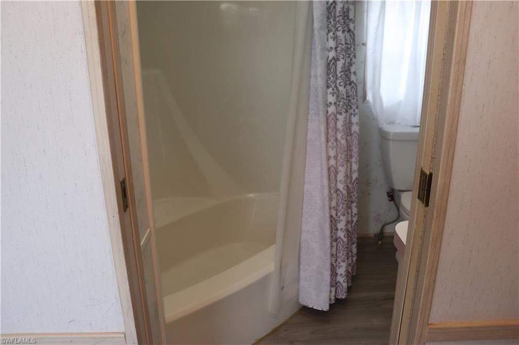 Full bath with toilet, a bathtub, a shower with shower curtain, and wood finished floors