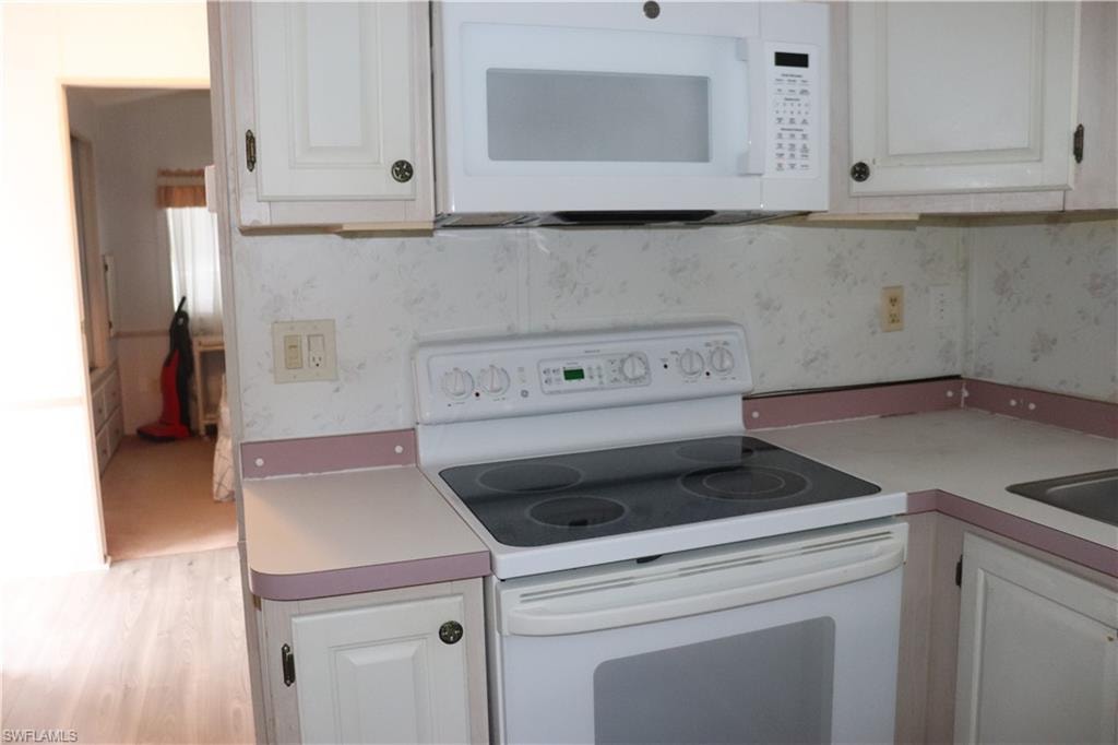 Kitchen with white cabinetry, light countertops, wallpapered walls, and white appliances