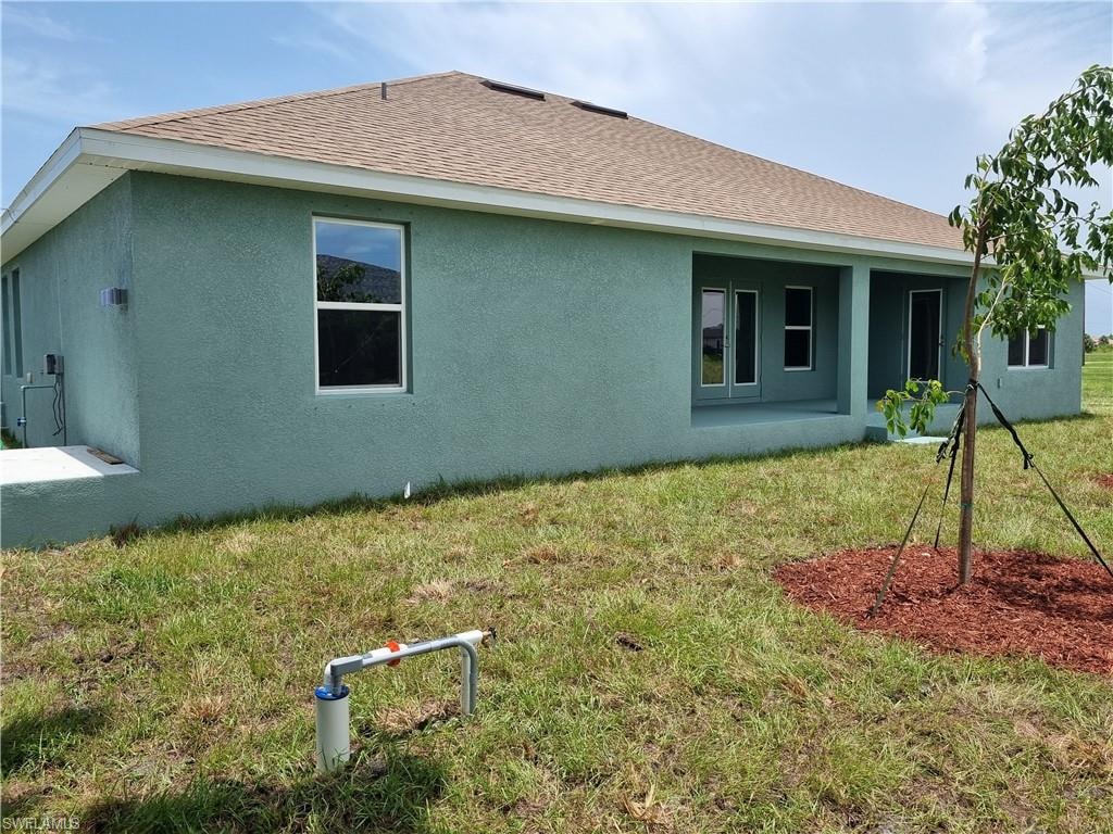 Rear view of property featuring stucco siding, a yard, and roof with shingles