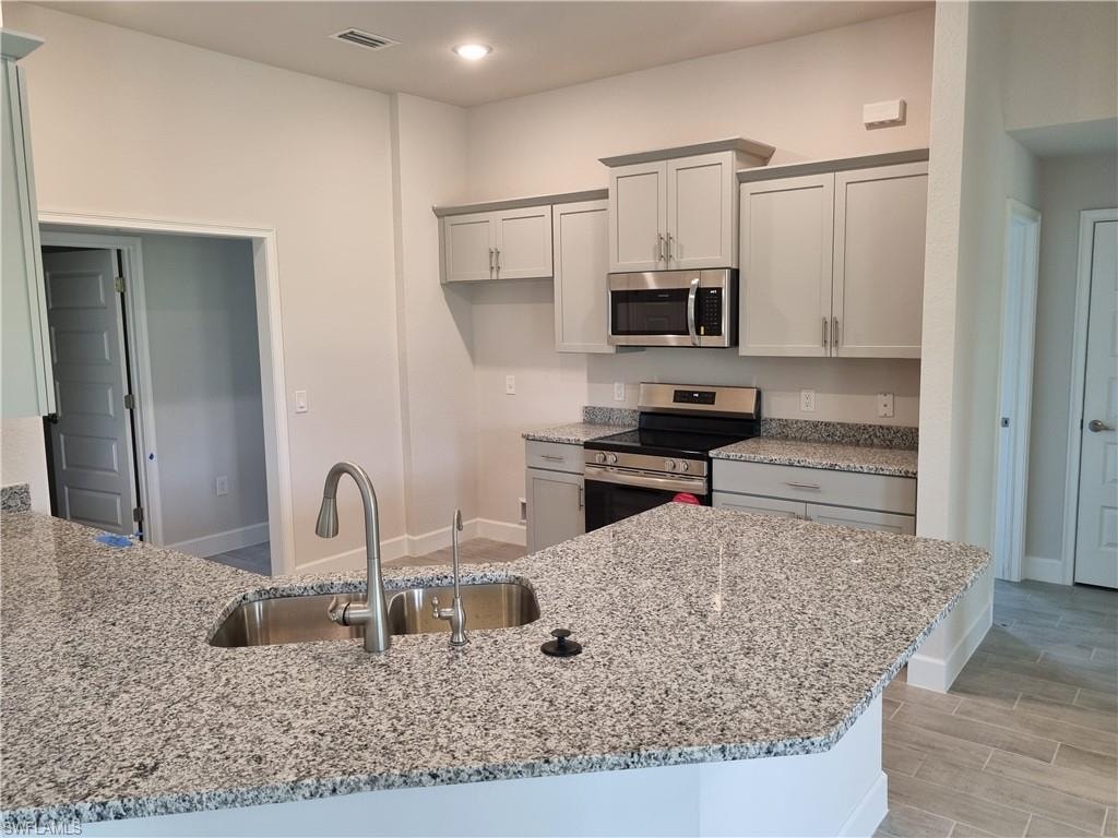 Kitchen with stainless steel appliances, light stone countertops, light wood-style flooring, a peninsula, and recessed lighting
