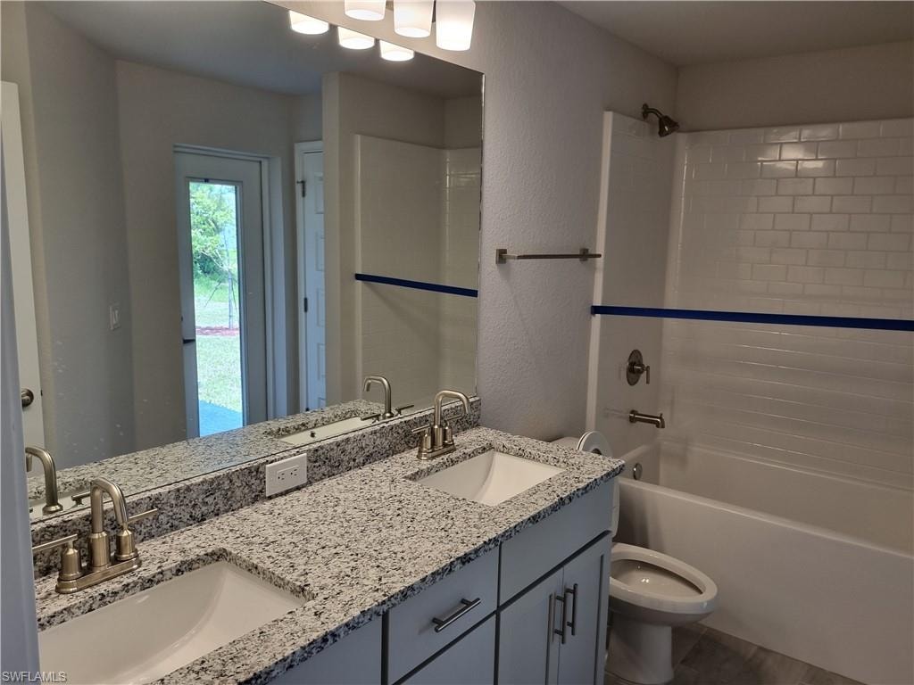 Full bathroom with double vanity, shower / bath combination, and a textured wall