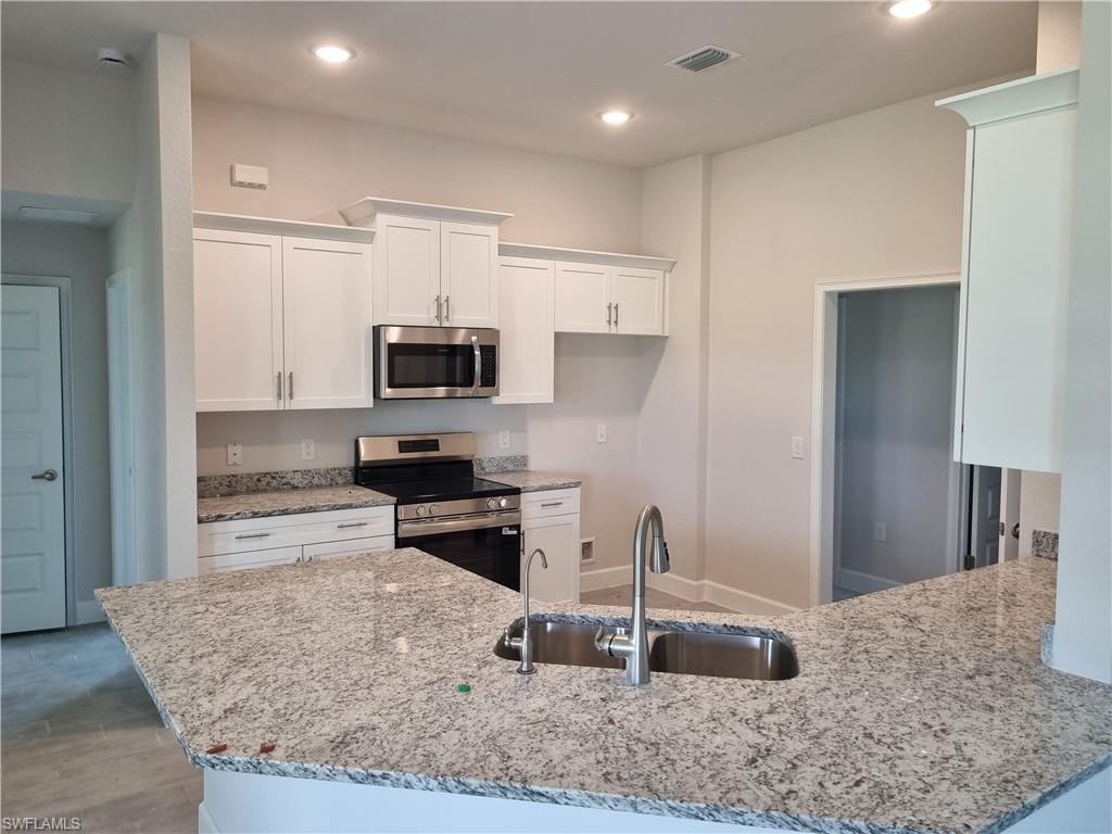 Kitchen with stainless steel appliances, light stone counters, white cabinetry, recessed lighting, and a peninsula