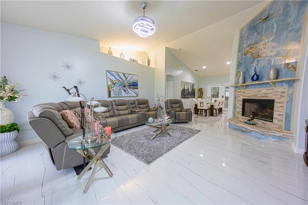 Living area with marble finish floor, a stone fireplace, high vaulted ceiling, and baseboards