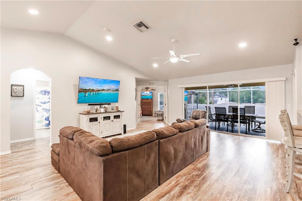 Living area with light wood finished floors, ceiling fan, arched walkways, and lofted ceiling