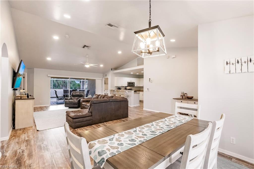 Dining room with vaulted ceiling, ceiling fan with notable chandelier, and light wood finished floors