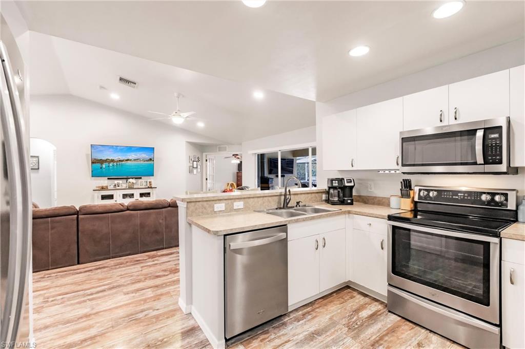 Kitchen with a peninsula, appliances with stainless steel finishes, lofted ceiling, a sink, and open floor plan