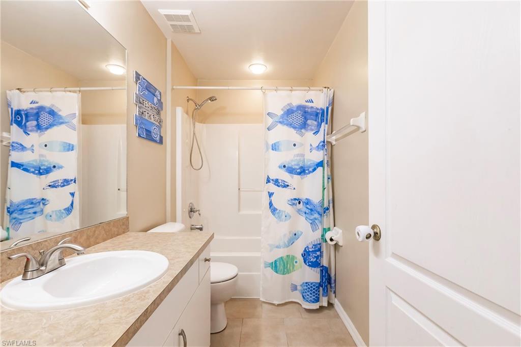 Bathroom with tile patterned flooring, vanity, toilet, visible vents, and shower / bath combo with shower curtain