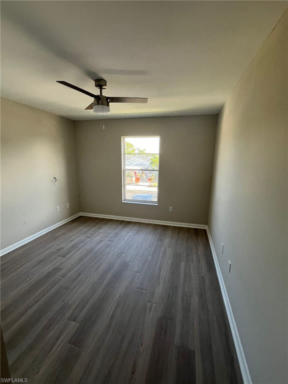 Spare room featuring dark wood-style floors, ceiling fan, and baseboards