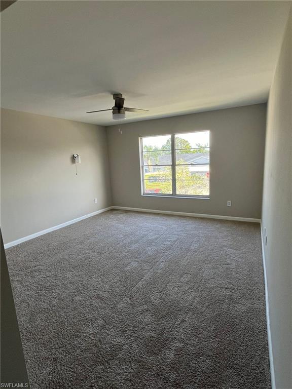 Empty room with carpet flooring, a ceiling fan, and baseboards