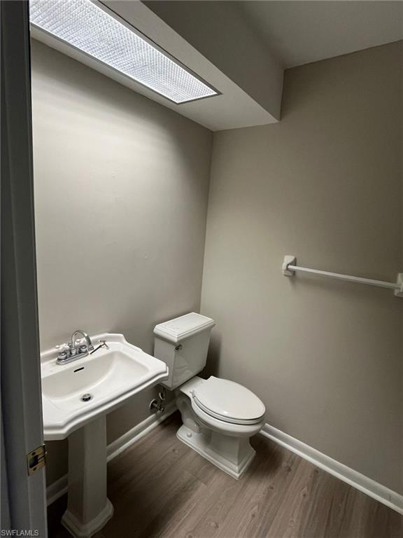 Half bath featuring baseboards, toilet, and wood finished floors