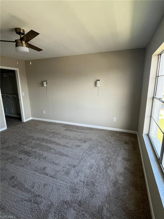 Empty room with baseboards, dark colored carpet, and ceiling fan