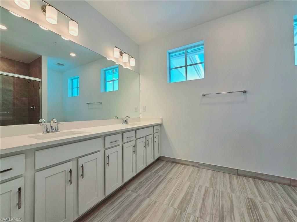 Bathroom with a stall shower, double vanity, healthy amount of natural light, baseboards, and recessed lighting