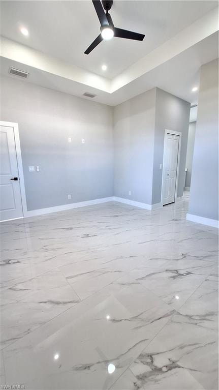 Spare room with a tray ceiling, light marble finish floors, a ceiling fan, and a towering ceiling