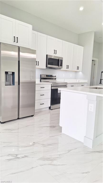 Kitchen featuring white cabinets, stainless steel appliances, pendant lighting, light marble finish flooring, and light stone countertops