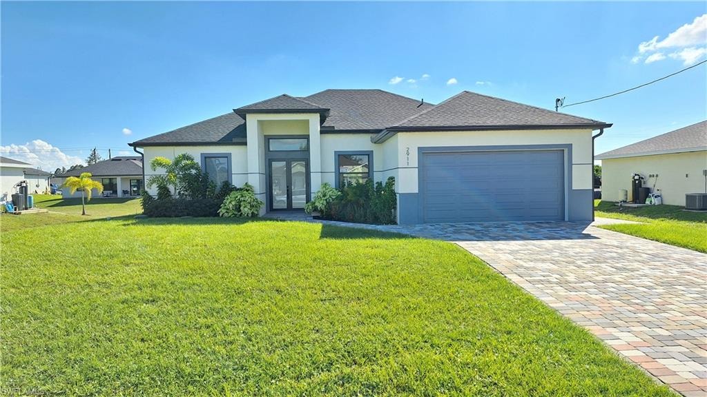 View of front of property with a front yard, stucco siding, a shingled roof, french doors, and decorative driveway