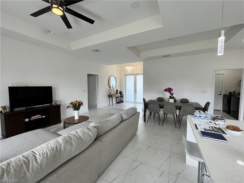 Living area with a raised ceiling, ceiling fan, and light marble finish floors