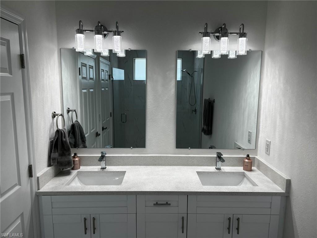 Full bath featuring double vanity, a shower stall, a textured wall, and a sink