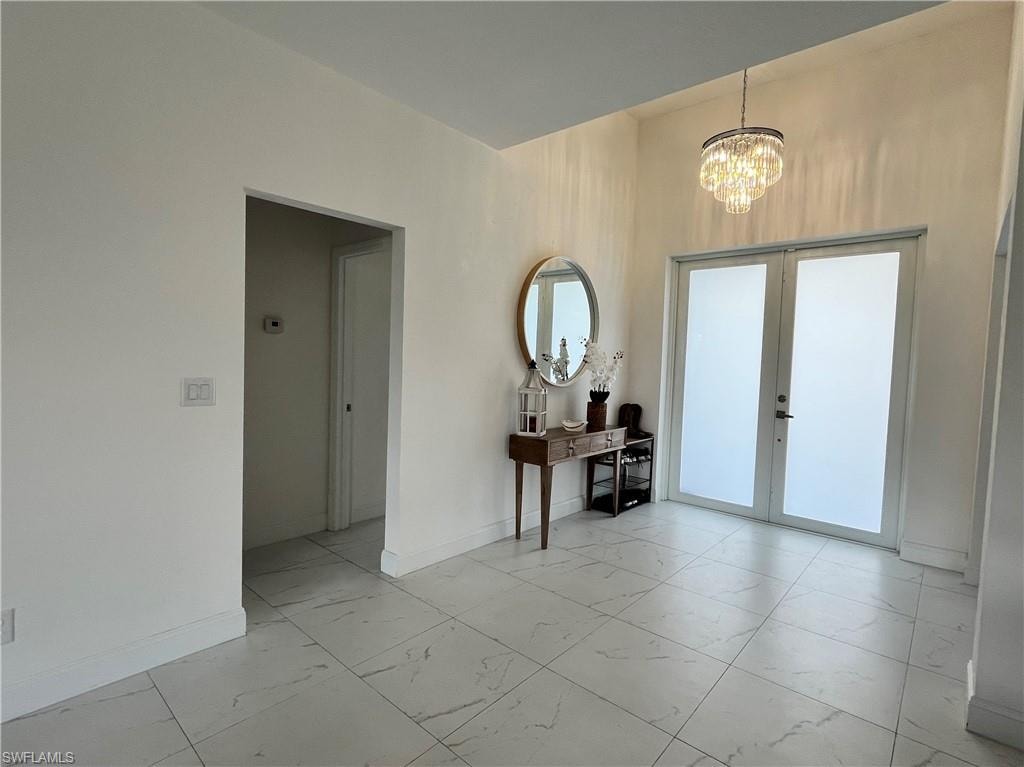 Foyer featuring light marble finish flooring, a chandelier, and french doors
