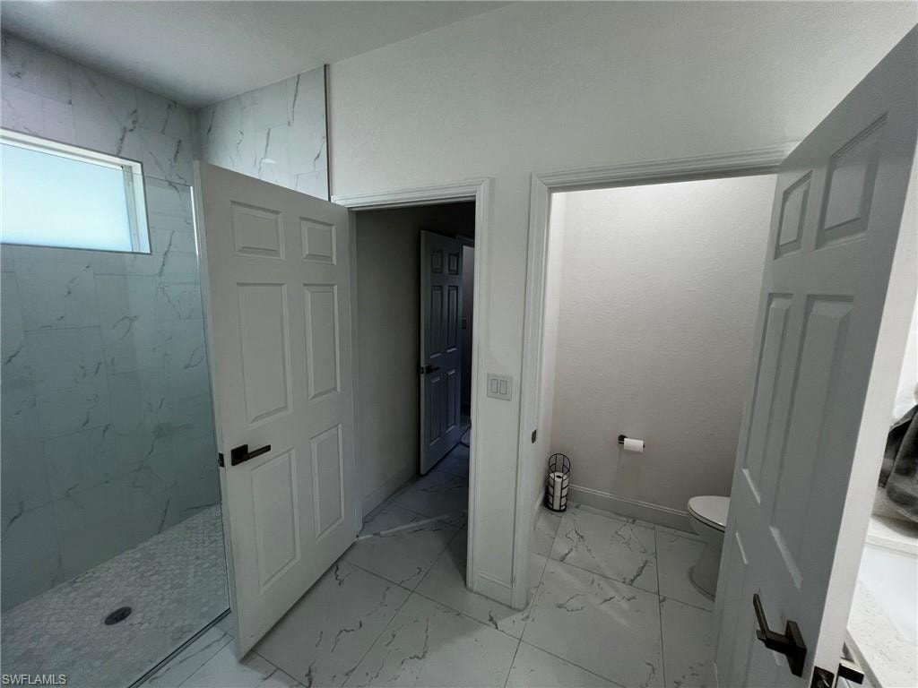Full bath featuring baseboards, marble finish floor, a marble finish shower, and toilet