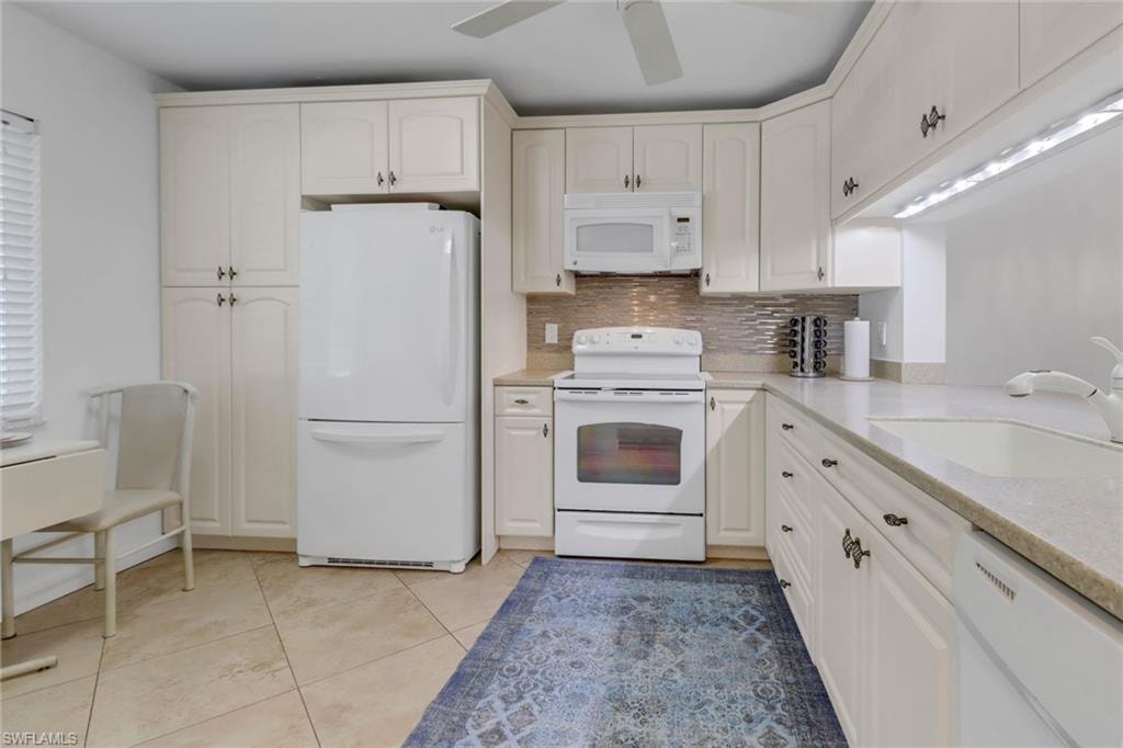 Kitchen featuring light countertops, backsplash, a sink, white appliances, and ceiling fan