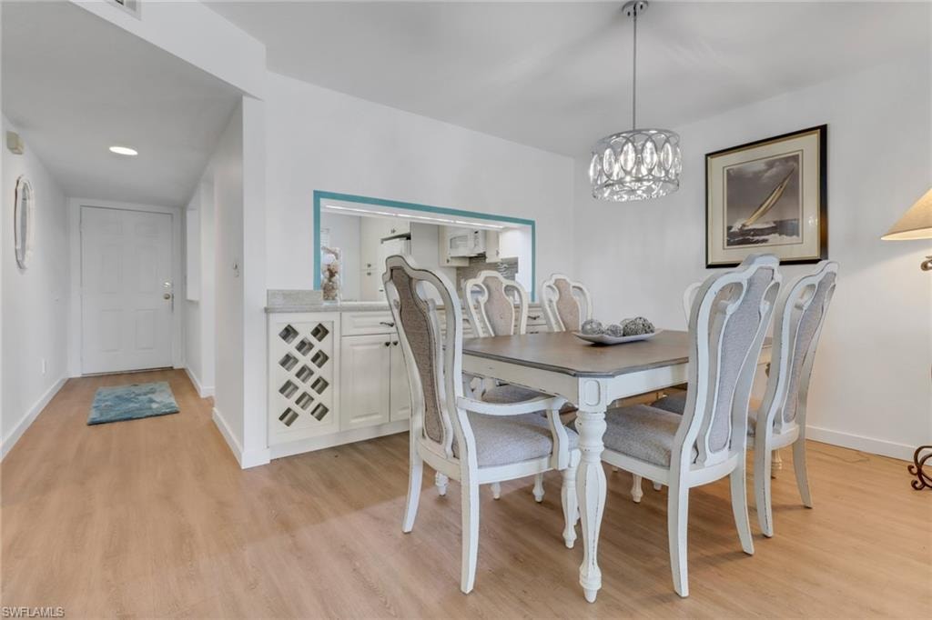 Dining area featuring a notable chandelier, baseboards, and light wood-style floors