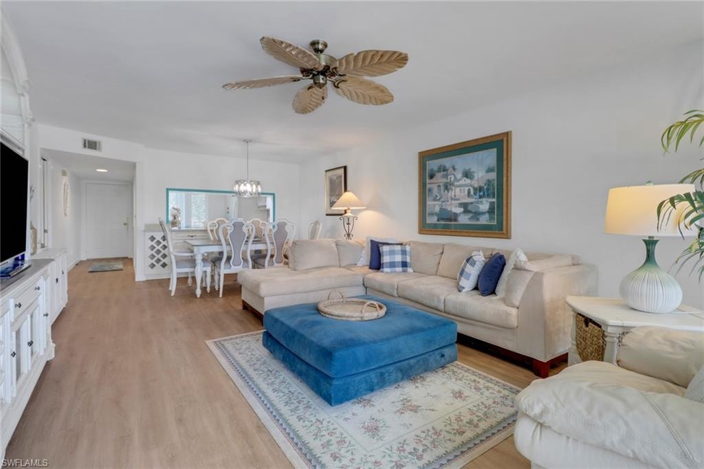 Living area with ceiling fan with notable chandelier, light wood-type flooring, and visible vents