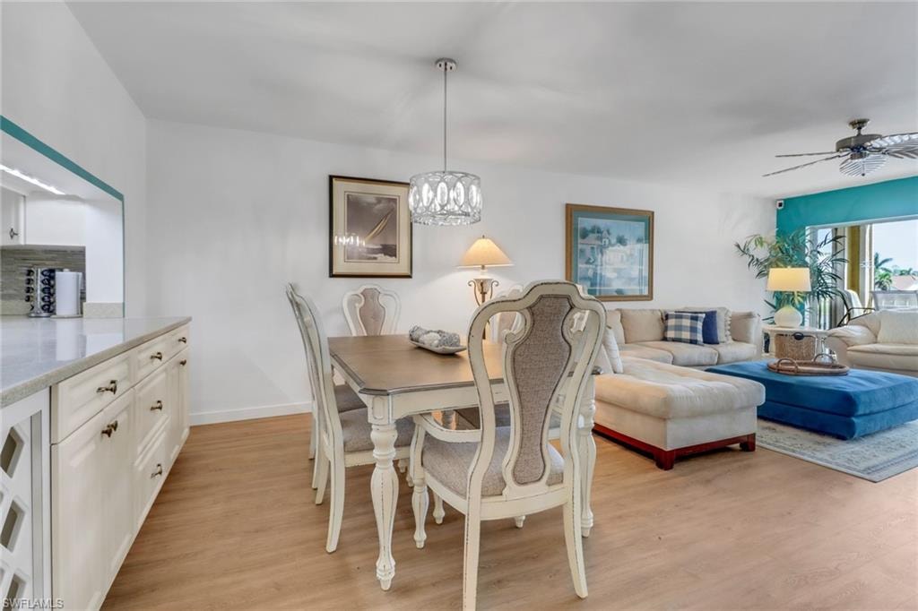 Dining space with light wood-style flooring, ceiling fan with notable chandelier, and baseboards