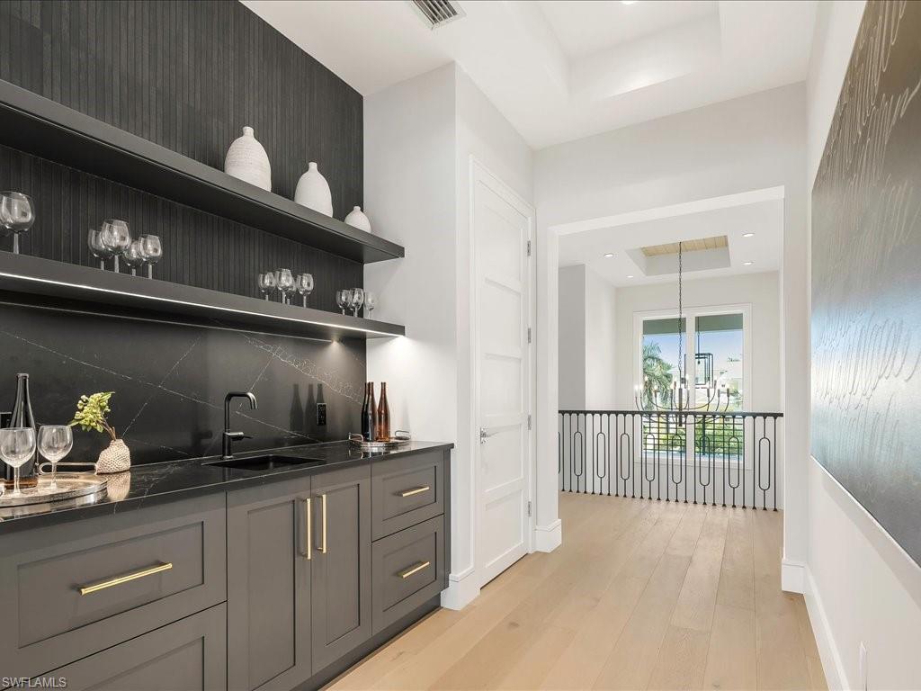 Bar featuring a tray ceiling, wet bar, decorative backsplash, a sink, and light wood-style floors