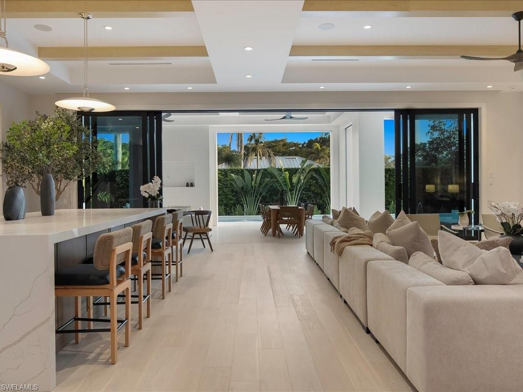 Living area featuring a ceiling fan, a raised ceiling, light wood finished floors, and recessed lighting
