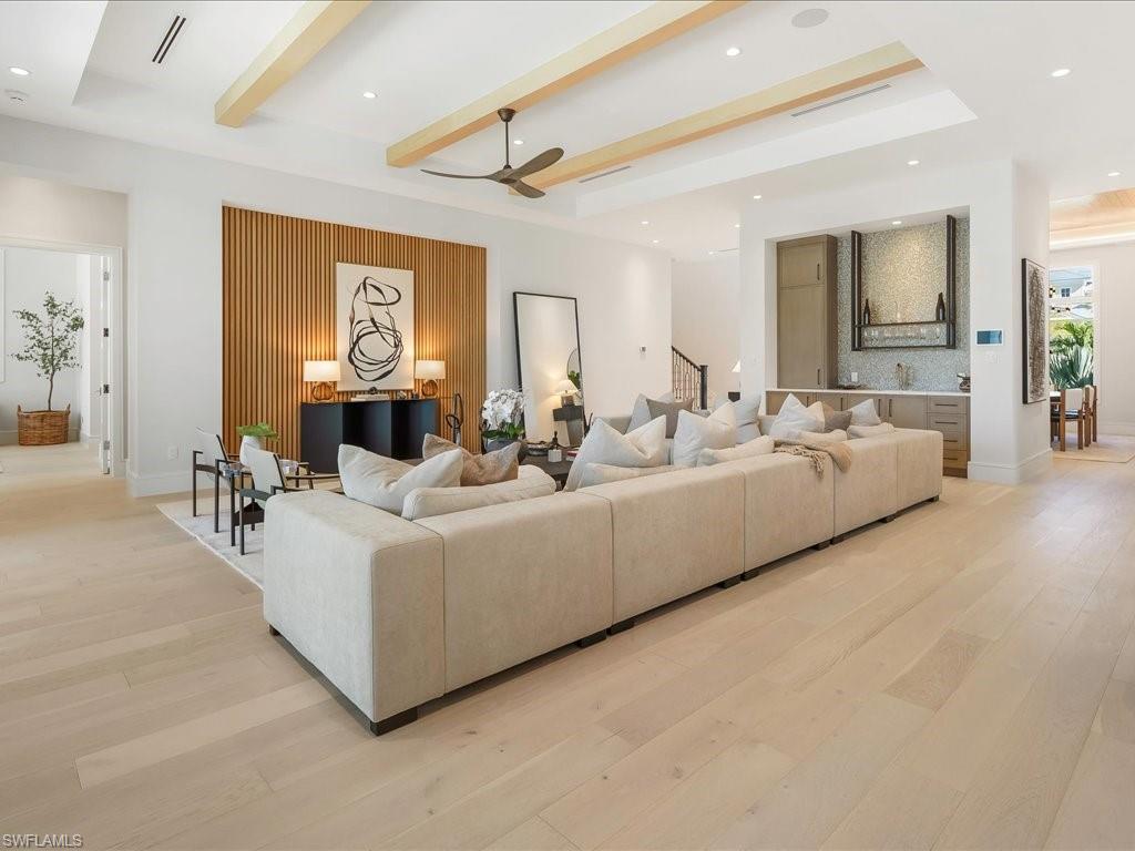 Living area featuring light wood-style flooring, beamed ceiling, stairs, a ceiling fan, and a raised ceiling