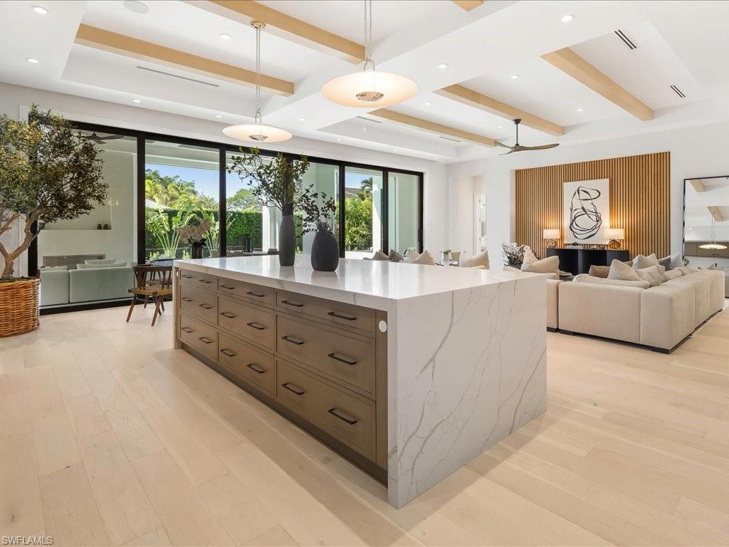 Kitchen featuring light stone counters, beam ceiling, hanging light fixtures, open floor plan, and light wood-type flooring