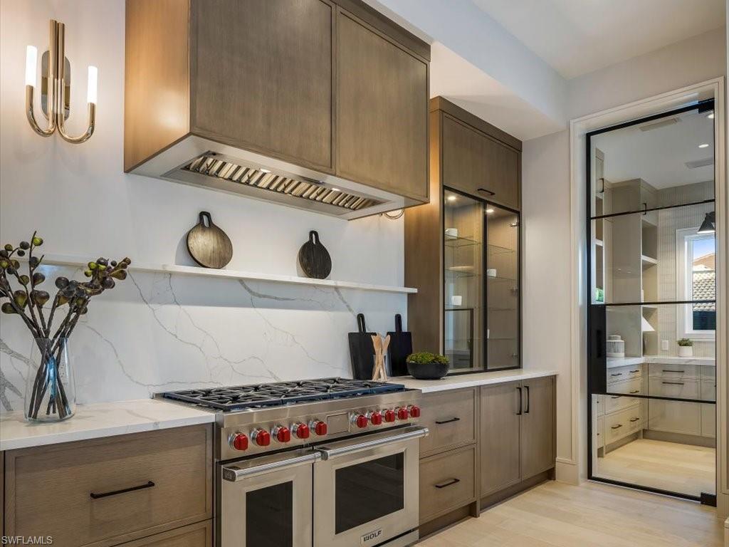 Kitchen with tasteful backsplash, open shelves, light wood-type flooring, light stone counters, and range with two ovens