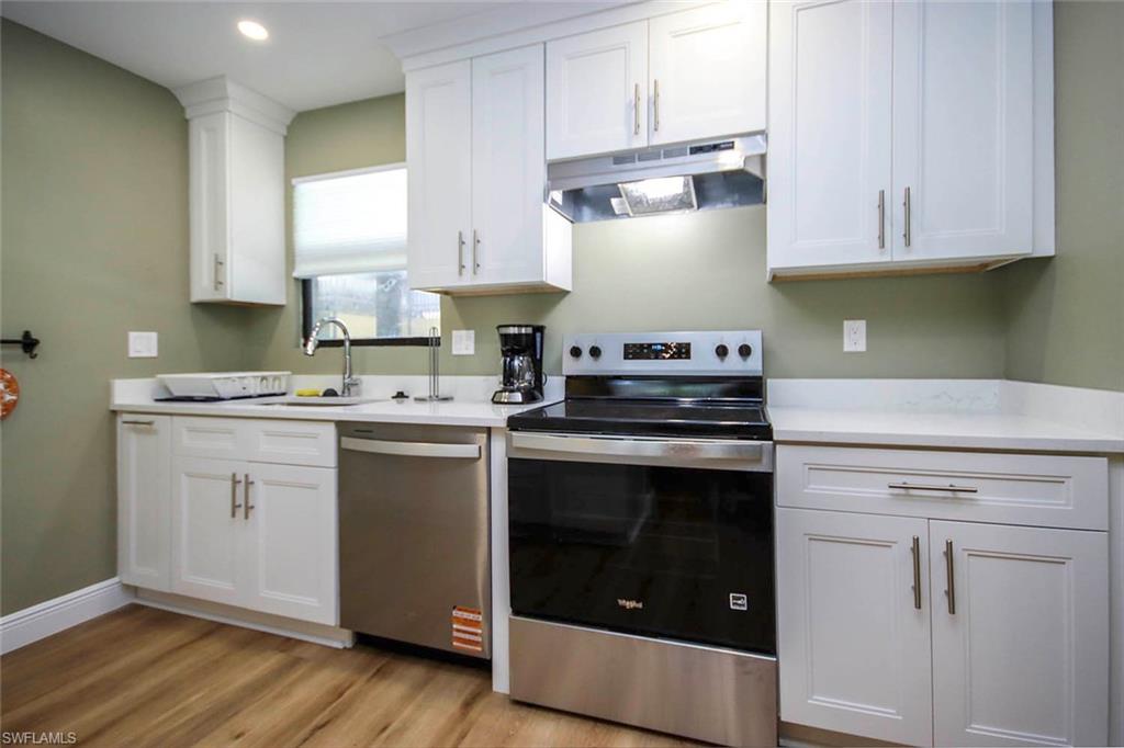 Kitchen featuring white cabinets, light countertops, stainless steel appliances, under cabinet range hood, and a sink