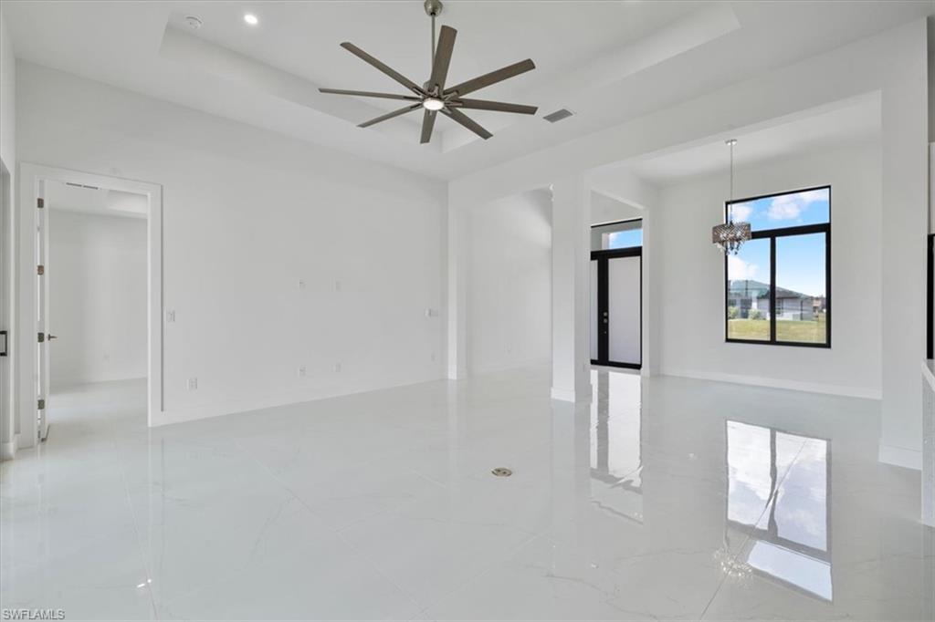 Unfurnished room featuring marble finish floor, ceiling fan with notable chandelier, visible vents, and a raised ceiling
